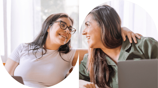 Two women smiling together while using a laptop